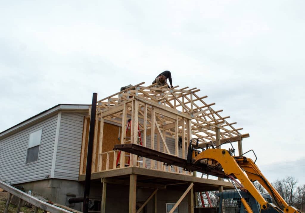 Carpenters on the roof of new building addition Unidentified carpenters work on the new roof, aided by some heavy equipment. Construction work is progressing nicely